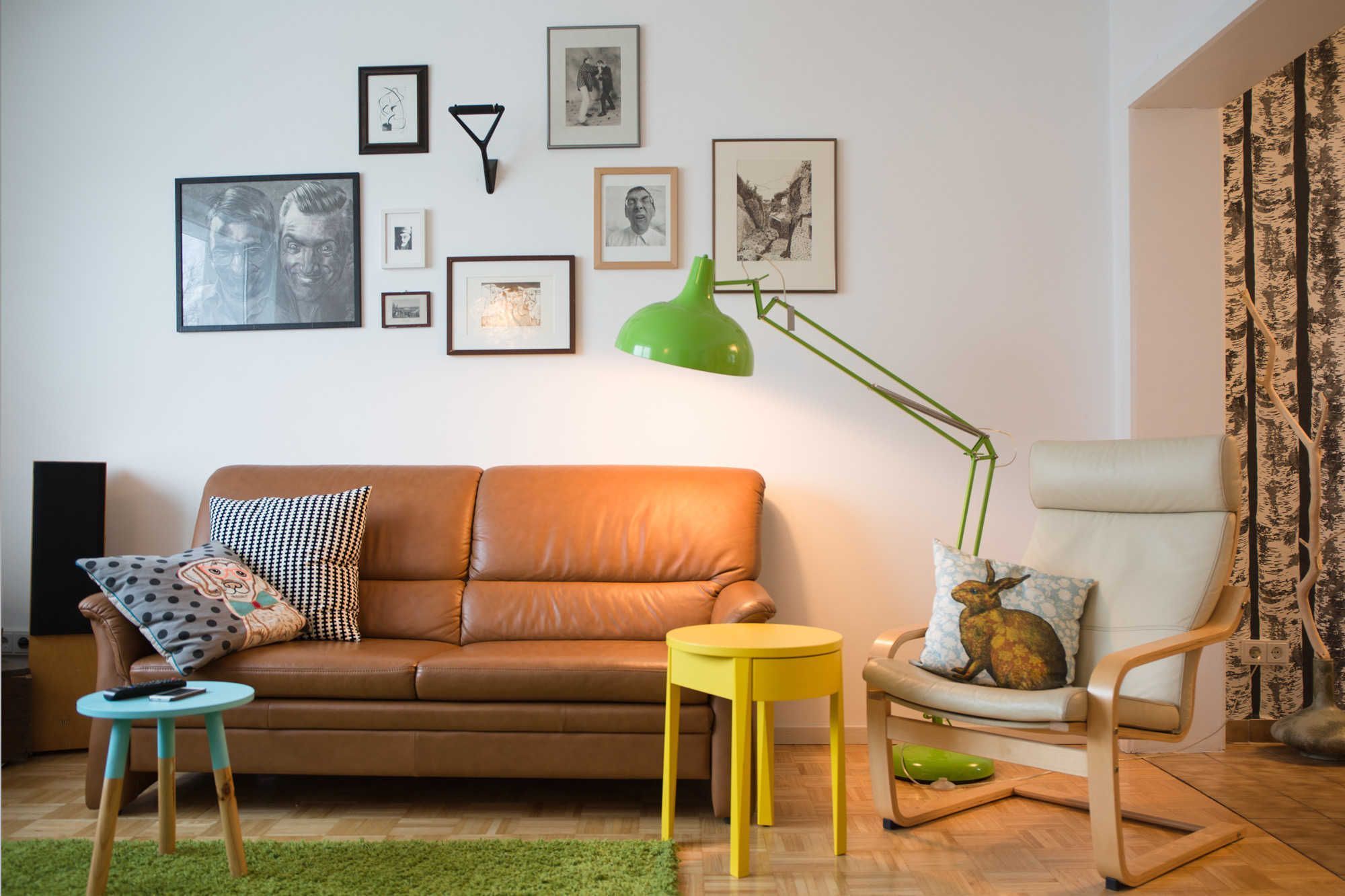 A living room with a brown sofa, a yellow table, a green floor lamp, a white armchair, and a small stool.
