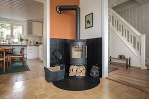 A modern kitchen with a wood-burning stove, a dining area with a wooden table and chairs, and a staircase. - Haushimmelblau, Germany (Sankt Andreasberg)