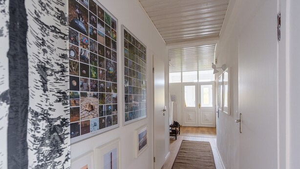 A hallway with a wooden floor, white walls, and a series of framed pictures on the left. - Haushimmelblau, Germany (Sankt Andreasberg)