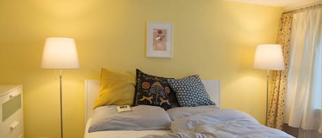 A bed with checkered bedding, two bedside lamps, a framed picture on the wall, and a window with curtains.