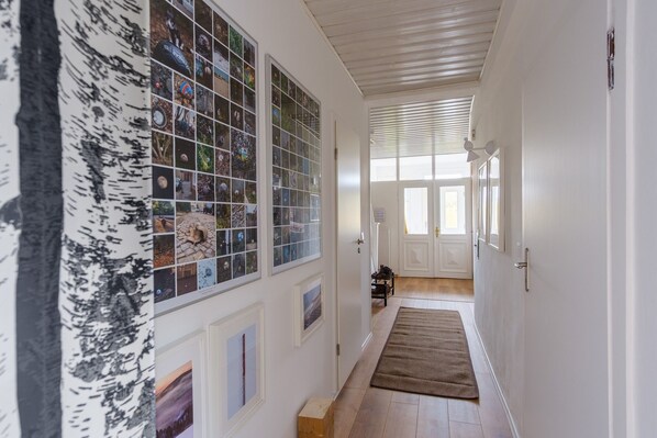 A hallway with a wooden floor, white walls, and a series of framed pictures on the left. - Haushimmelblau, Germany (Sankt Andreasberg)