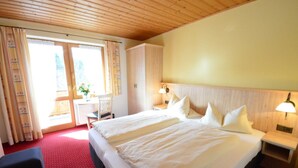 Et hotelværelse med to senge, trælofter, et rødt tæppe, en træskab, et natbord med lampe og et vindue med gardiner.