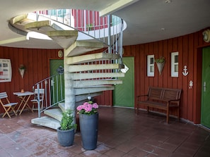 A spiral staircase with a metal railing, a bench, and potted plants in a room with wooden walls and tiled flooring. - 3-room apartment - Holiday Park in Plau (Plau am See)