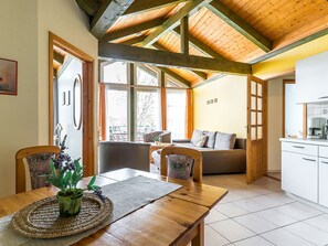 A dining area with a wooden table, chairs, and a woven placemat. There is a sofa in the background with a view of the outdoors. - 3-room apartment - Holiday Park in Plau (Plau am See)