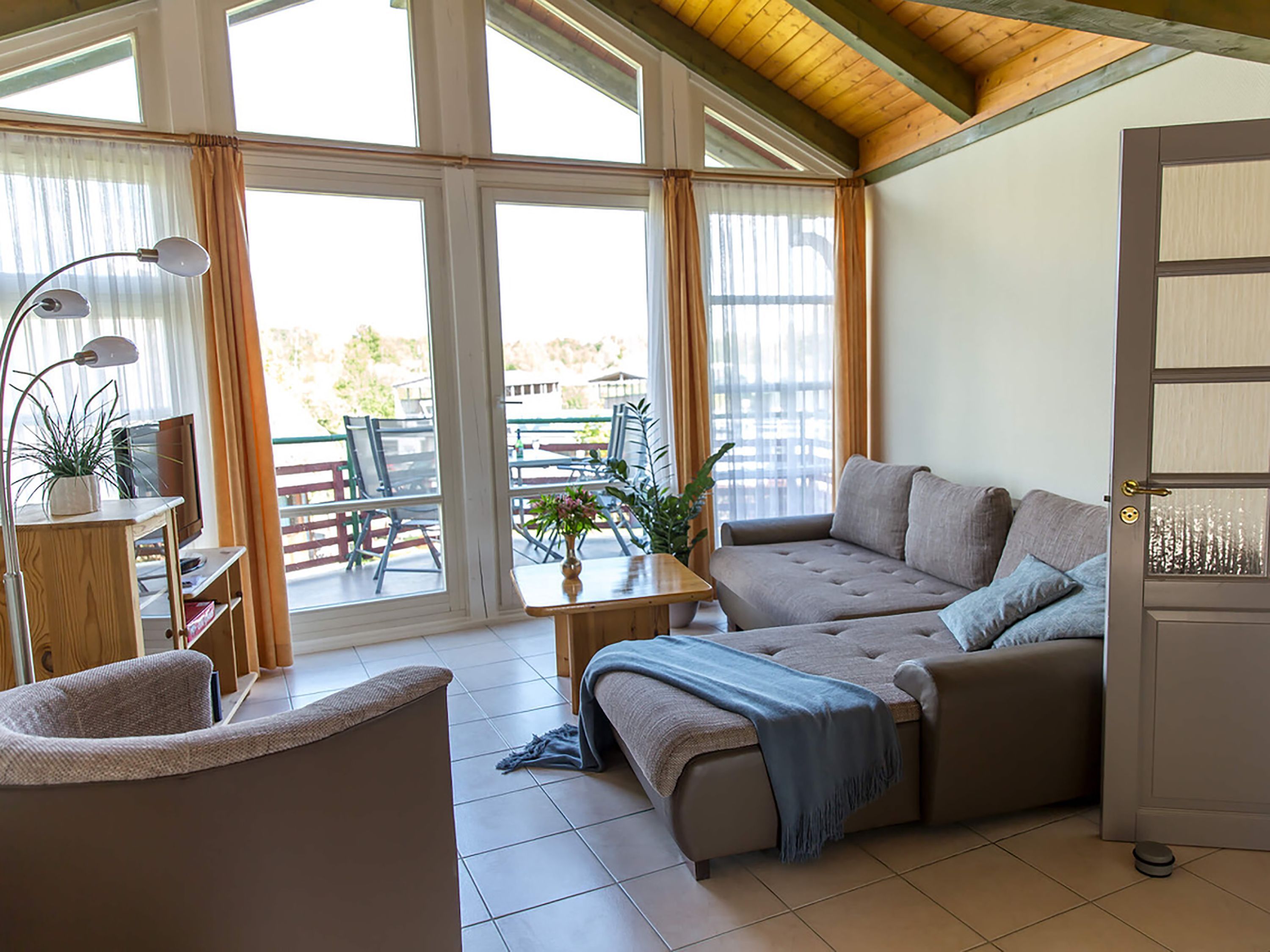 Ein gemütliches Wohnzimmer mit einer Couch, einem Sessel, einem Tisch mit Pflanze und einem Fernseher.