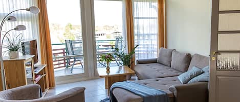 A cozy living room with a sofa, a chair, a table with a plant, and a television.