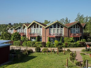 Une rangée de maisons en briques, dotées de grandes fenêtres et de balcons, et entourées d’un jardin bien entretenu.