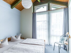 A bedroom with two beds, a chair, a lamp, and a window with curtains.