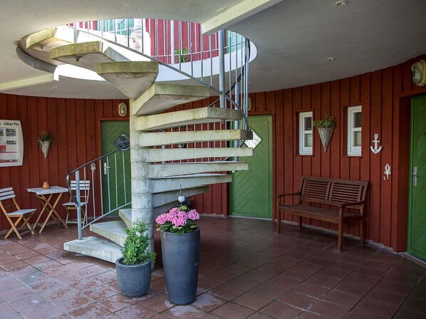 A spiral staircase with a metal railing, a bench, and potted plants in a room with wooden walls and tiled flooring.