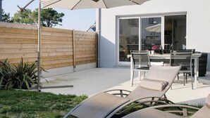 Un patio con mobiliario exterior, una valla de madera y una puerta corrediza de vidrio que da a un espacio interior.