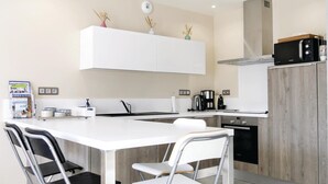 Una cocina moderna con armarios blancos, una isla central con taburetes y vajilla Bosch, además de un microondas.