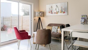 Una sala de estar moderna con un mueble de vidrio corredero que da a un balcón, un sofá, una silla roja, una mesita y una estantería.
