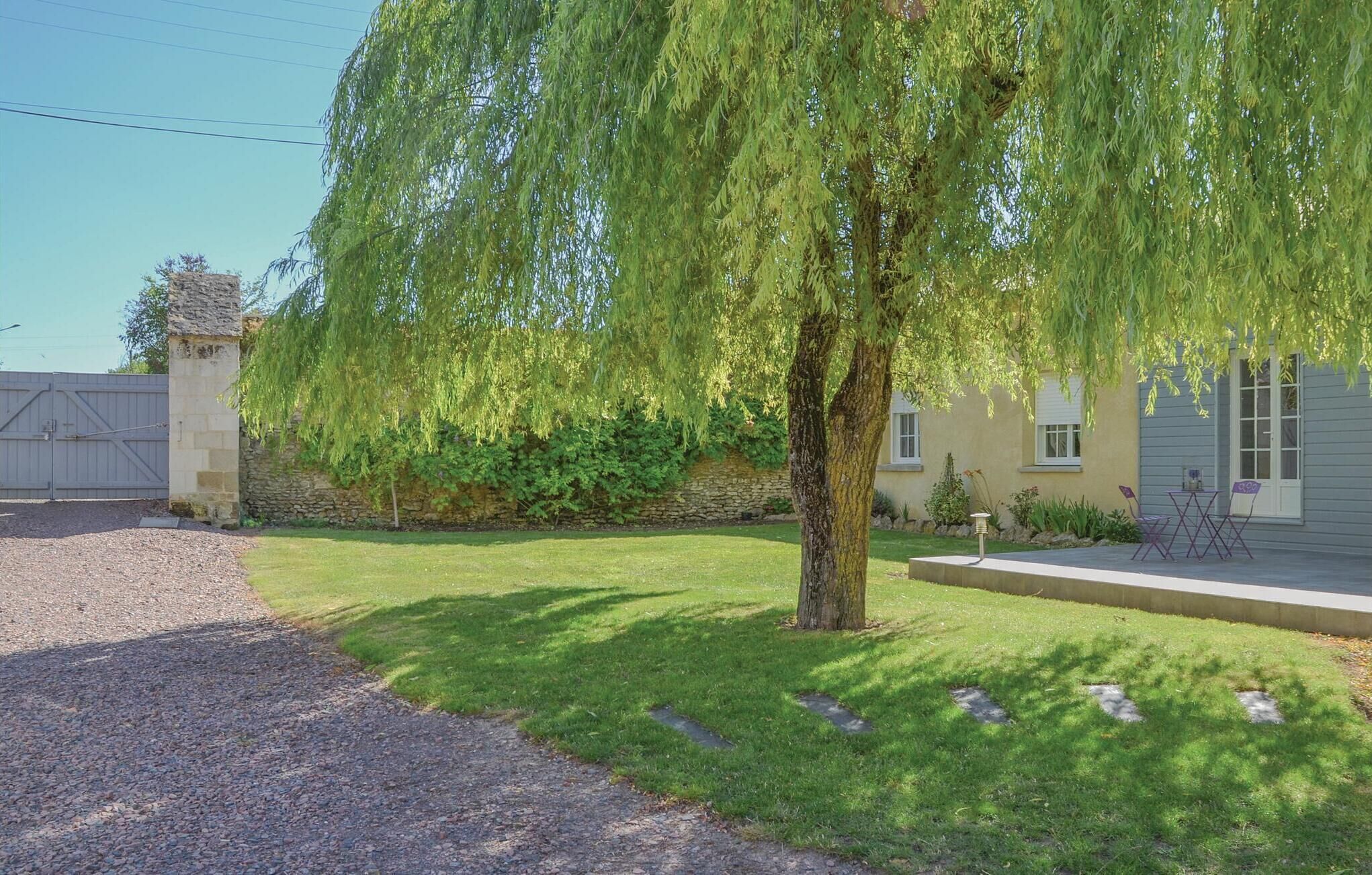 Propiedad residencial con muro de piedra, sauce llorón y camino de entrada de grava.