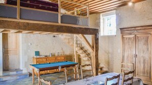 Una habitación amplia con mesa de billar, muebles de madera y una escalera que lleva a un nivel superior.