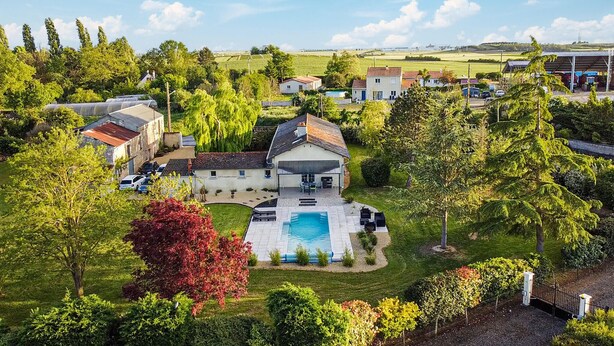 Una casa grande con piscina, rodeada de vegetación exuberante y otras viviendas.