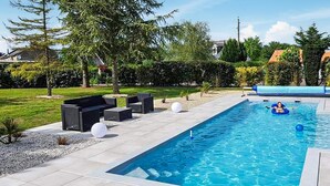 Una piscina rectangular con superficie de agua azul cristalina, rodeada por una zona de solárium con mobiliario exterior.