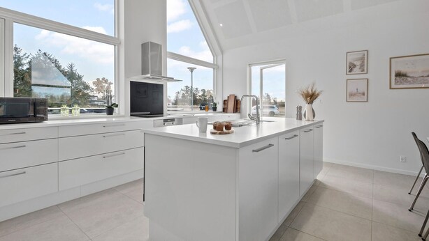 Una cocina moderna con una isla grande, armarios blancos y vistas al exterior.