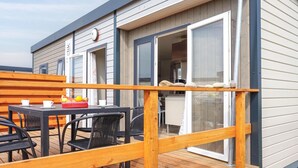 A deck with a table and chairs, a wooden railing, and a window with a view of the interior.