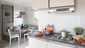 A modern kitchen with a gas stove, a dining area with a white table and chairs, and a built-in shelf with decorative items.