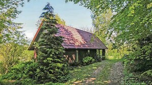 Un chalet rustique avec un toit en pente, entouré d’une végétation luxuriante et accessible par un chemin de gravier.