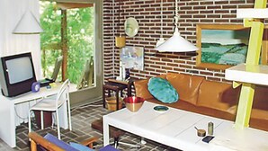 Une pièce avec un mur en briques, une table blanche, un canapé marron, un téléviseur et une fenêtre donnant sur un paysage verdoyant.
