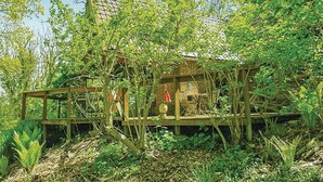 Un chalet rustique doté d’une terrasse en bois, entouré d’une végétation luxuriante et d’arbres.