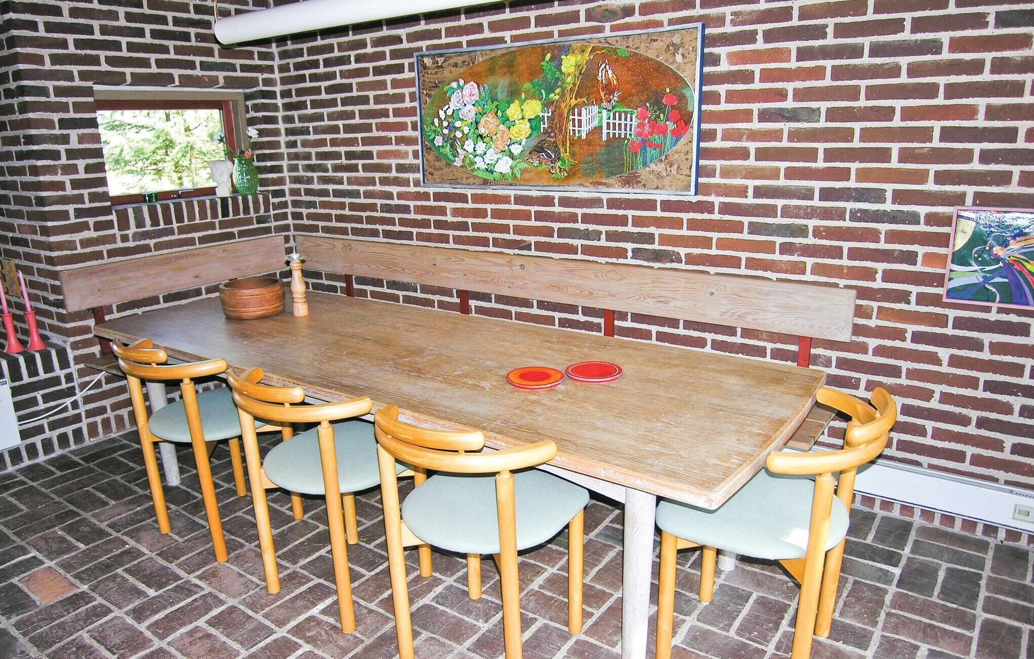 A rustic dining area with a wooden table and chairs, a bench, and a brick wall with a mural.