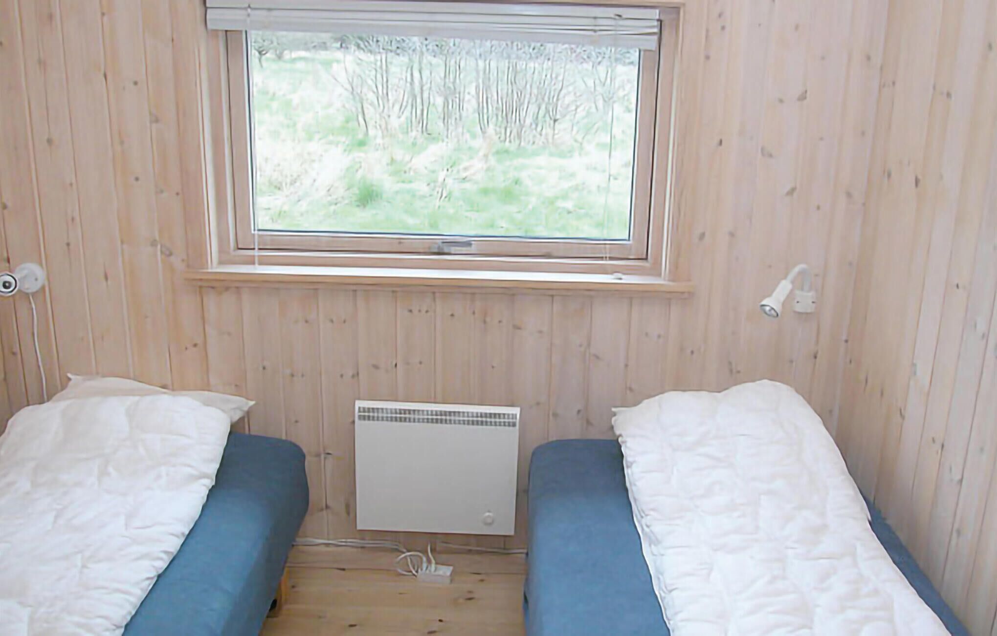 A small room with two beds, a window, and a wall-mounted heater.