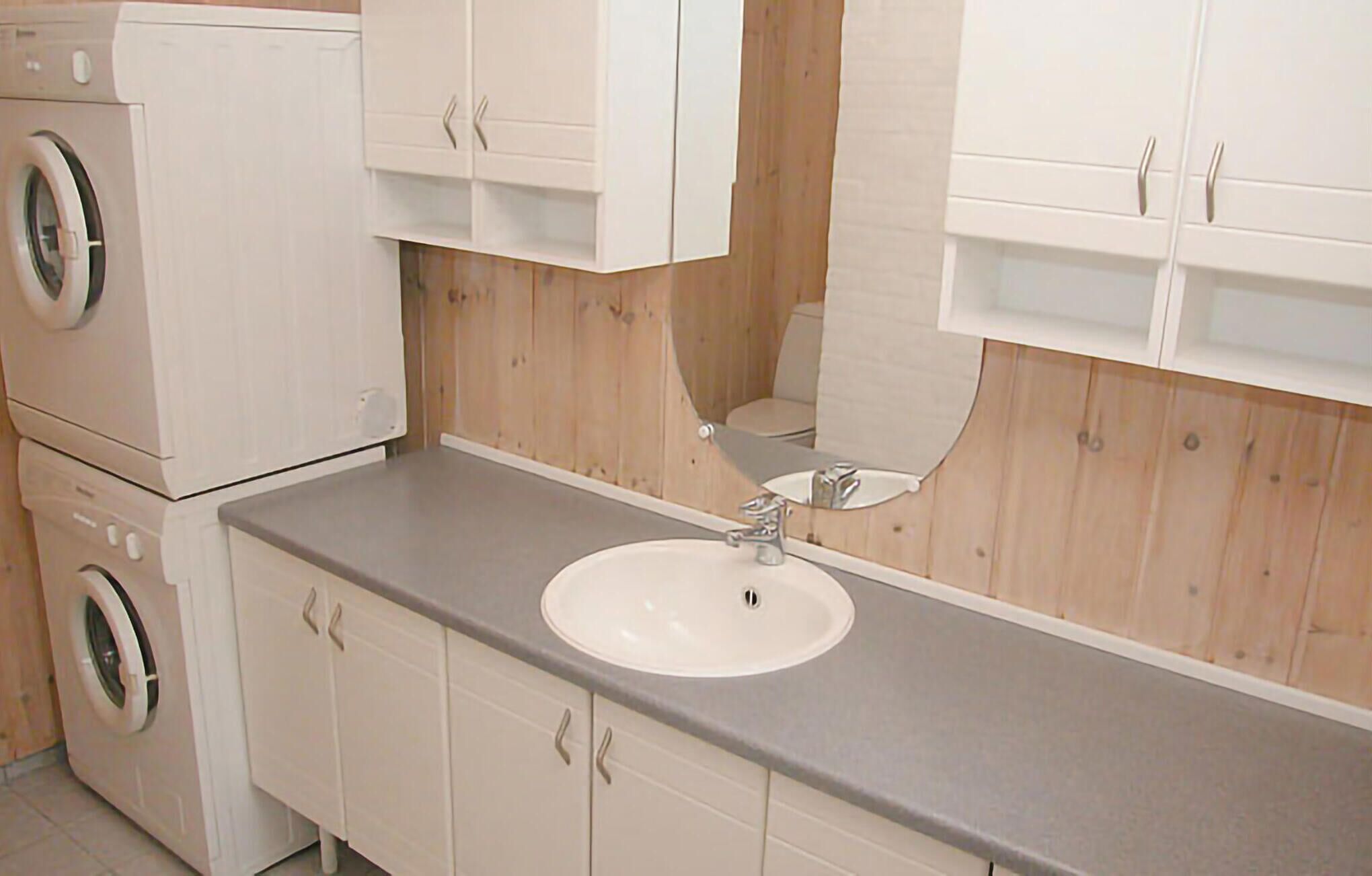 A compact bathroom with a sink, mirror, and a washing machine.