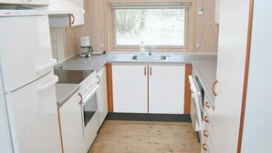 A compact kitchen with white cabinets, a built-in oven, a coffee maker, and a window above the sink. - Cozy home in Aakirkeby with sauna (Aakirkeby)