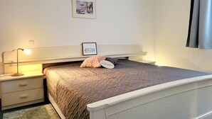A bedroom with a single bed, a bedside table with a lamp, a framed picture on the wall, and a window with curtains. - (146) 2-room apartment - Apartment house Olymp (Kühlungsborn)