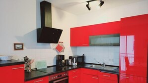 A kitchen with red cabinets, a black stove, and a microwave. - (146) 2-room apartment - Apartment house Olymp (Kühlungsborn)