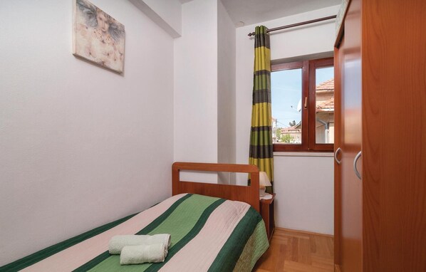 A small, neatly arranged bedroom with a single bed, a wooden headboard, a window with a striped curtain, and a painting on the wall. - 2 bedroom cozy apartment in Split (Split)