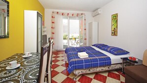 Una habitación de hotel con piso a cuadros, cama con ropa de cama azul, mesa de comedor con mantel estampado y un cuadro en la pared.