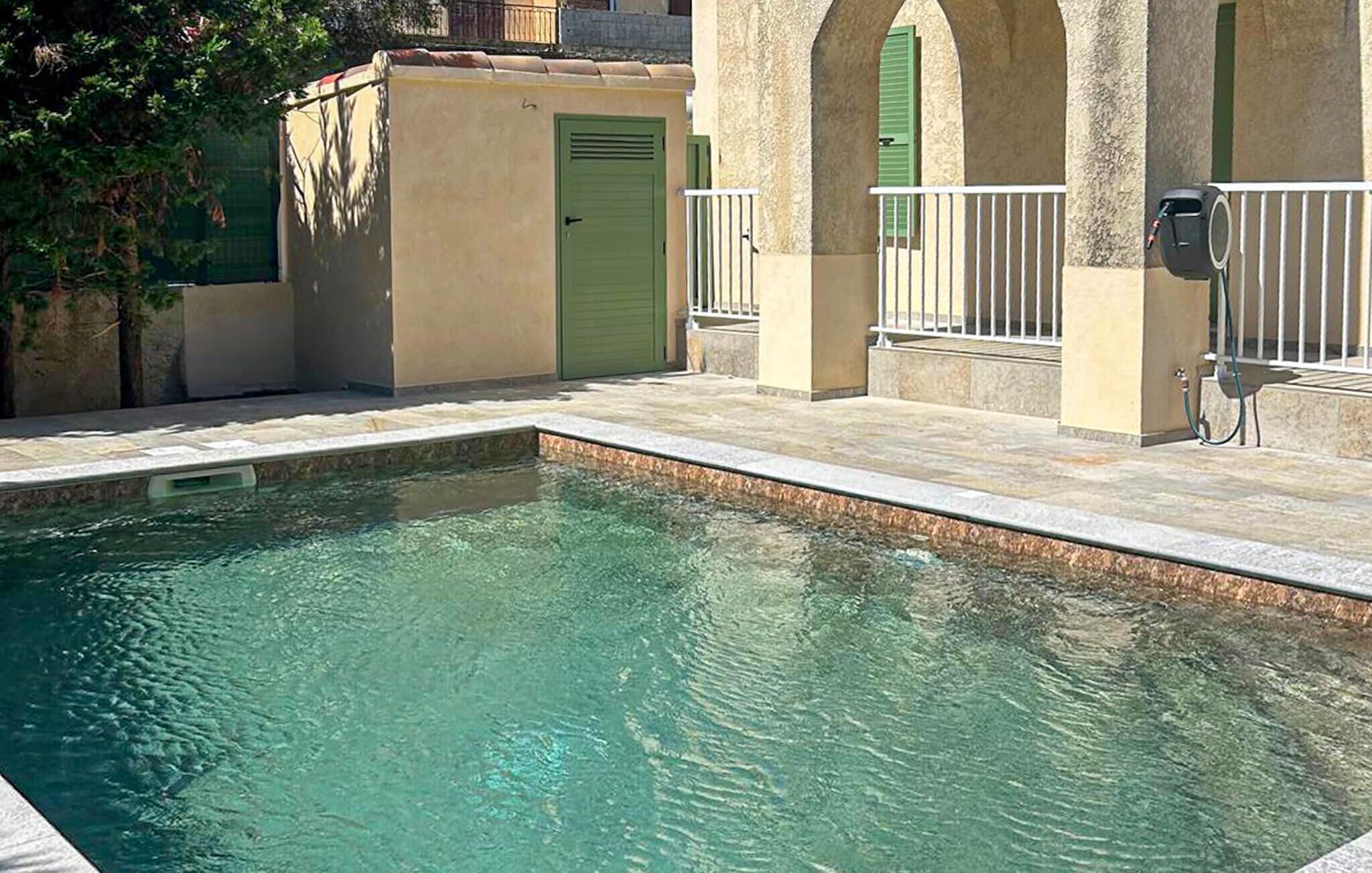 A swimming pool with a stone border, a green door, and a white railing.