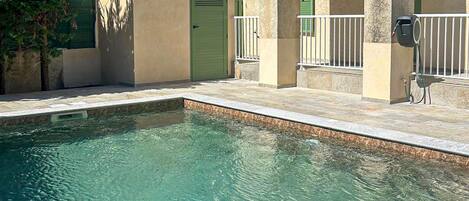 A swimming pool with a stone border, a green door, and a white railing.