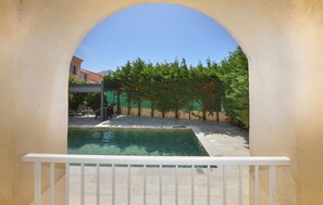 Une piscine dotée d’une balustrade blanche, entourée d’une terrasse avec des chaises et un espace salon abrité.