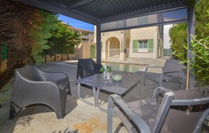 Une terrasse extérieure avec une table et des chaises, une piscine et une vue sur des bâtiments dotés d’arcades.
