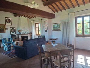 Una sala de estar con sofá, una mesa de comedor con sillas, chimenea y cuadros en las paredes.