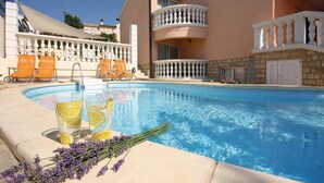 Piscina com cadeiras de descanso laranja, um guarda-corpo branco e uma parede de pedra.