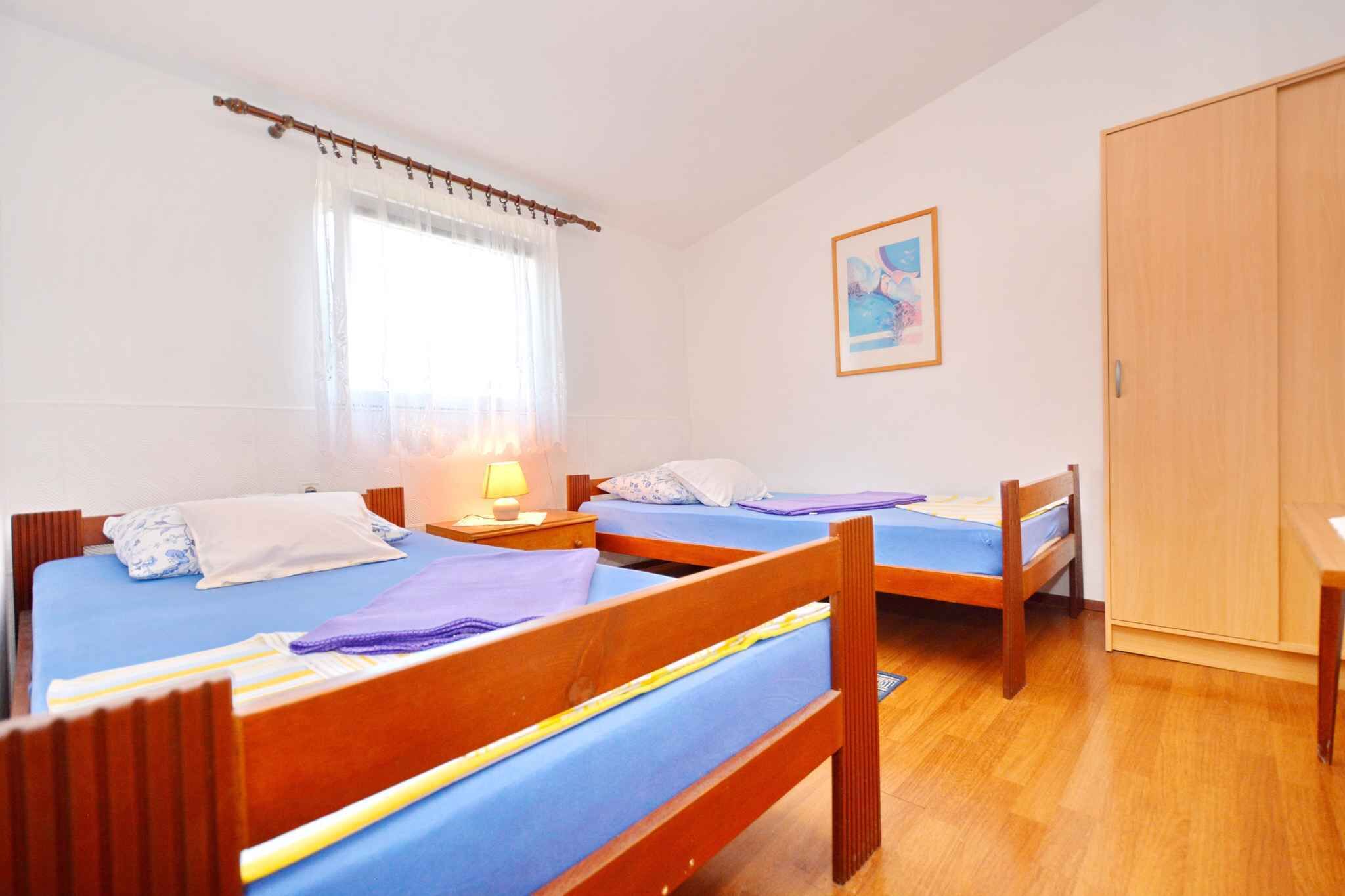Una habitación con dos camas de madera, un armario de madera, una ventana con cortinas traslúcidas y un cuadro enmarcado en la pared.
