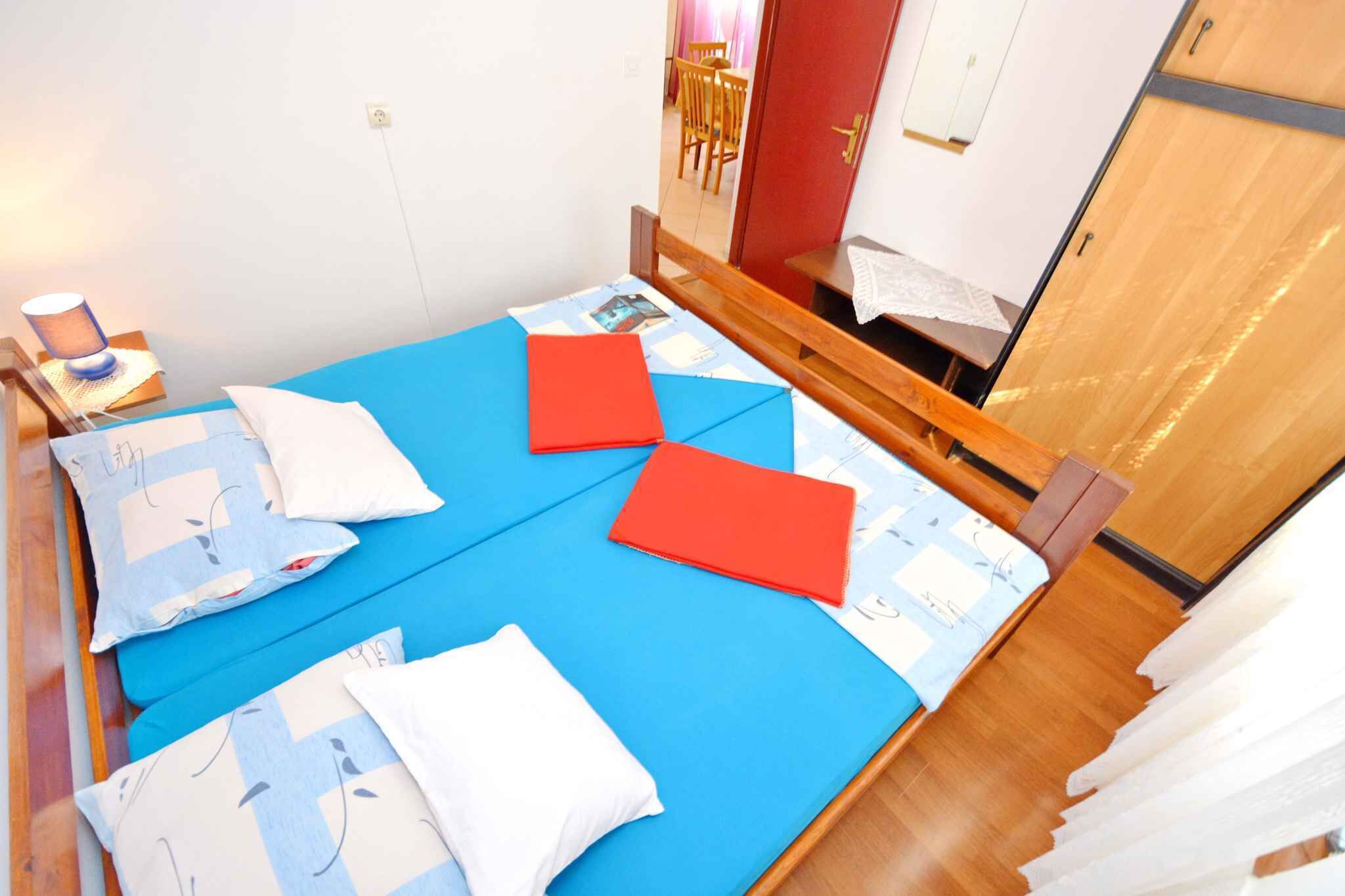 Cama bem arrumada com roupa de cama azul e branca, cabeceira de madeira e uma pequena mesa de cabeceira com abajur.