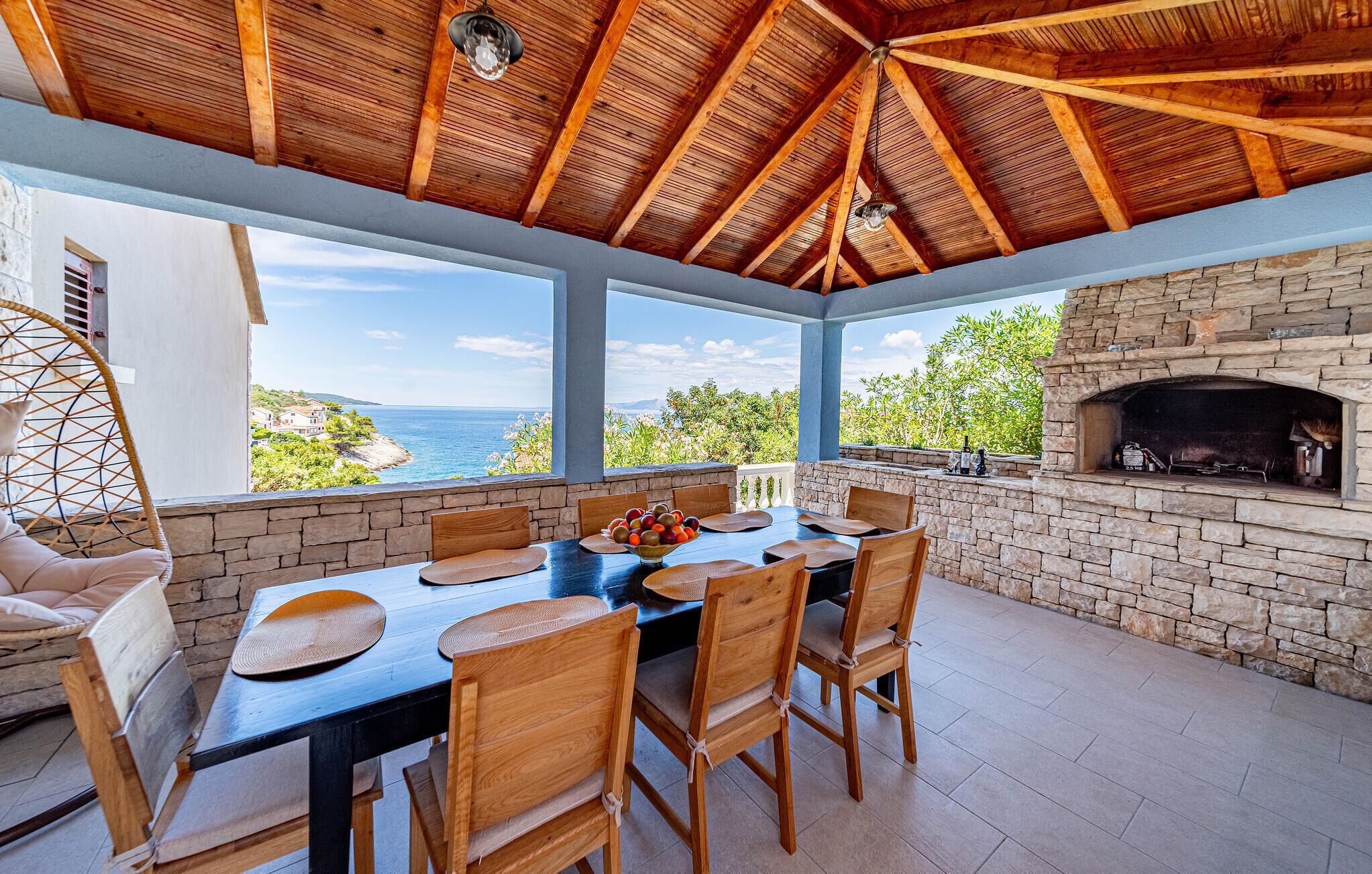 An outdoor dining area with a stone fireplace, wooden chairs, and a table set for four.