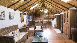Ein rustikales Interieur mit einem hohen, reetgedeckten Dach, Korbmöbeln, einem Glastisch und einer Küchenzeile mit Holzausbau.