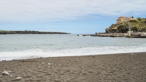 Ein Strand mit felsigem Ufer, einem Steg und einem Gebäude auf einer Klippe.