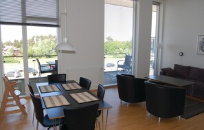 Cozy living space with a dining table for four, large windows, and a comfortable sofa.