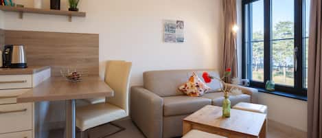 A modern living room with a sofa, a coffee table, a dining table, and a kitchen area with a kettle.