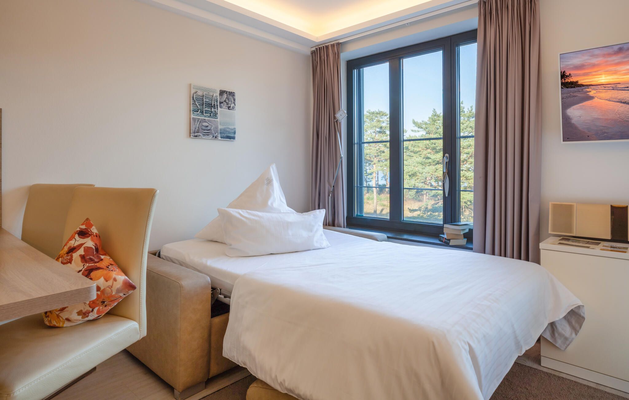 A hotel room with a bed, a sofa, a window with a view of trees, and a painting on the wall.