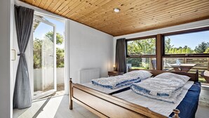 A bedroom with a wooden bed, a window with curtains, a radiator, and a view of the outdoors.
