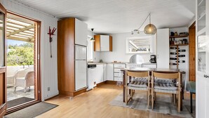 A modern kitchen with white cabinets, a wooden dining table, and a hanging light fixture.